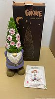Photo of the GNOME solar light statue showing the colorful gnome with flower-decorated hat, standing in front of original box and instruction leaflet.