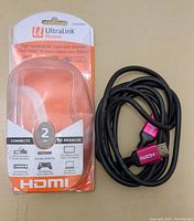 Photo of the HDMI cable outside packaging with clear view of black cable and pink HDMI connectors. Packaging indicating 2 meter length and HDMI features.