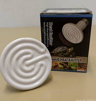 Ceramic heat emitter bulb placed in front of its box, showing the spiral filament design of the bulb.