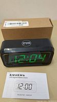 Photo showing the Kwanwa digital alarm clock in front of a cardboard box and the instruction manual displaying the model number KW618.