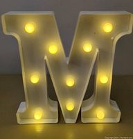 Front view of the white LED letter M illuminated with 11 warm white bulbs glowing.