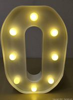Front view of white letter O with six round LED bulbs illuminated, showing warm yellow glow.