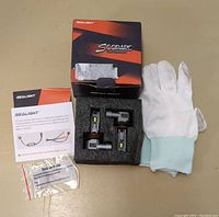 Photo of the SCOPARC LED bulbs, white protective gloves, wiring harness, installation instructions, and original packaging box showing Sealight branding.