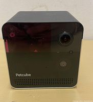 Front view of the black cubic Petcube Smart Camera with lens, speaker, and brand logo visible on the front panel.