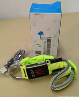 Photo showing the neon yellow LED dog collar with ON/OFF label, metal ring, quick-release clasp, USB charging cable, and original box.