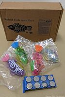 Four robot fish cat toys in assorted colors with battery pack in front and box behind