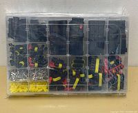 Top view of transparent plastic organizer box filled with various tool kit accessories including black plastic connectors, red and yellow clips, yellow rubber seals, and small metal terminals or screws.