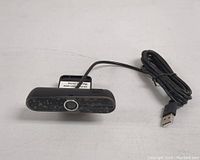 Front view of black USB webcam with lens and attached cable.