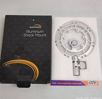 Photo showing black Auphonix product box with branding and product name 'Aluminum Shock Mount' alongside the shock mount in protective foam packaging.