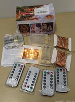 Photo showing four transparent battery compartments, two coiled strands of copper wire fairy lights, five remote controls laid out, original box with holiday images, and instruction sheet.