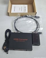 Top-down photo showing black HDMI converter box labeled 'HDMI Converter HDMI TO HDMI+ AUDIO', USB power cable, power adapter, HDMI cable, and user manual inside an open cardboard box.