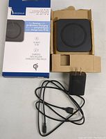 Black Insignia wireless charging pad in cardboard packaging, with included power adapter and USB cable, alongside product box showing 10W Qi wireless charging details.