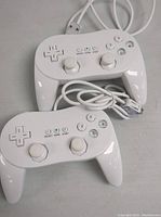 Two white Nintendo Wii Classic Controller Pro wired controllers tangled with cables, showing button layout and ergonomic grips