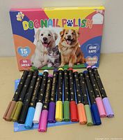 Full view of the 15 colorful dog nail polish pens arranged in front of the product box featuring dogs and a cat with colorful branding and product claims like 'skin safe' and 'vivid colors'.