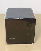 Front view of the Petcube smart camera showing the lens, sensors, and Petcube logo on a black cube device.