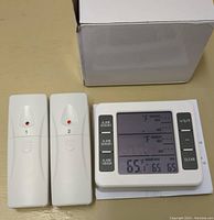 Digital thermometer with two remote sensors and white box in background, showing front LCD and buttons.