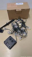 Solar Christmas lights string with clear bulbs, green wiring, small solar panel, and ground stake, displayed next to its cardboard box.
