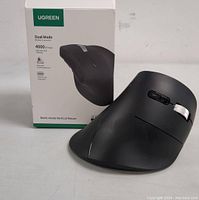 Front view of black UGreen vertical mouse with box in background showing brand logo and product name.
