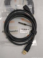 Coiled black USB 3.0 extension cable with packaging visible underneath showing branding and product details.