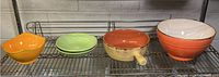 Four ceramic and porcelain bowls in different colors and shapes on metal shelf.