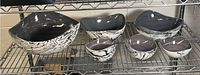 Side view of entire salad bowl collection on metal shelf showing one large bowl with marbled black and white exterior and six smaller matching bowls
