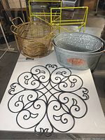 Overview of all metal decorative items including the black wall hanging, galvanized container with label, gold basket, and yellow rack.