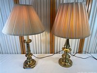 Pair of brass table lamps turned on, showing the difference in size and same shade style.