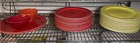 Shelving unit with stacks of ceramic plates and bowls in red, yellow, and orange colors arranged side by side.