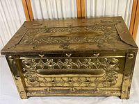 Front angled view showing the top and front brass embossed panels with ornate design and aging wear.