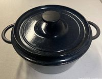 Full view of oval dark blue sparkly enameled cast iron casserole with lid and handles.