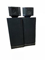 Photo of front of two tall black speakers with black cube speakers on top.