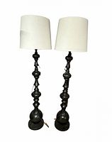 Photo showing front view of both floor lamps with white drum shades on black metal decorative bases.