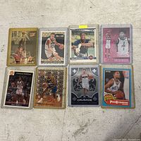 Top-down photo of 8 assorted basketball cards on floor background showing front of each card