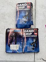 Three boxes of hand grip strengtheners, two labeled BAG Hand Grip Strengthener with 'NO EXCUSES' text and one with 'Adjustable Resistance' text.