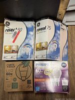 Four boxes of LED bulbs showing GE Reveal 60W and 75W, Bits Bulb 60W LED, and Philips 2-pack 60W equivalent LED bulbs.