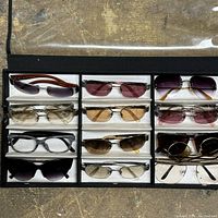 Full view of the black display case containing 12 pairs of assorted designer sunglasses arranged in rows