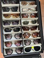 15 pairs of assorted designer sunglasses in a black display case, showing different styles and colors.