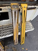 Front view of two yellow metal saw horses with foldable legs, showing rust and paint wear.