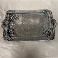 Top view of rectangular silver serving tray with grape clusters and leaves design along edges.