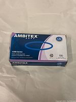 Front and top views of the Ambitex V200 Series vinyl exam gloves box showing brand, size, quantity, and series details.
