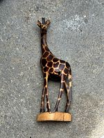 Full body image of a wooden giraffe figure standing on a natural wood base with painted spots.