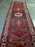 Full-length view showing geometric medallion pattern on red and navy field with ivory border