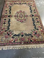 Full view of the rectangular wool rug showing beige base, central floral medallion, multi-colored floral border, and fringe.
