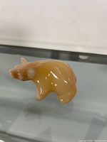 Angle view of the polished stone bear figurine showing the bear's side with visible smooth surface and light brown and tan coloration.
