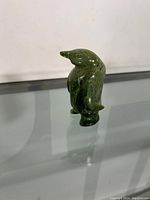 Front side view of green stone penguin figurine on reflective glass surface.