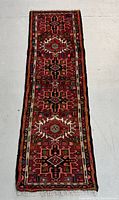 Full view of rectangular hand knotted wool Persian rug runner with rich red background and geometric pattern.
