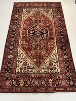 Full view of the Persian Zanjan wool rug showing the rectangular shape with central medallion and surrounding motifs in rust red, cream, and black colors.