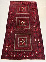 Full view of rectangular Persian Baluch wool rug showing three central square medallions on vibrant red background bordered with geometric and floral patterns.