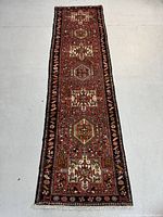 Full-length view of runner rug showing red field with repeating medallions and dark border