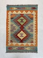 Full view of rectangular Persian kilim rug, showing colorful geometric pattern and fringed edges.